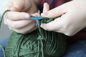 Hands holding knitting needles and yarn making a stitch Hands holding knitting needles and yarn making a stitch